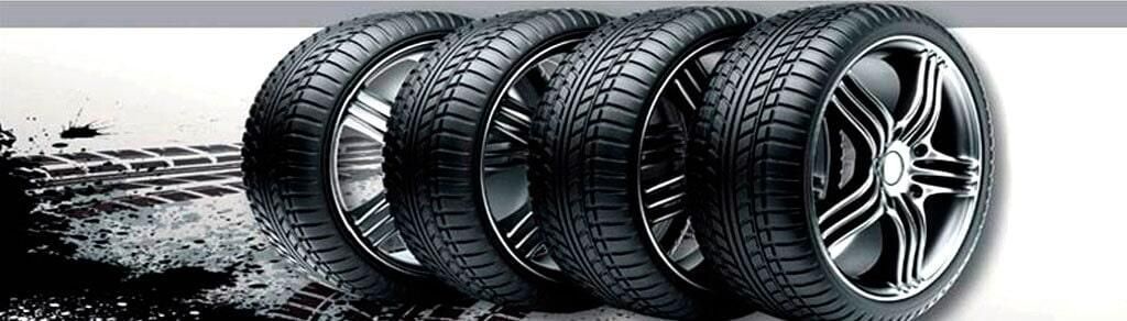 Cinco neumáticos negros en fila con diferentes diseños de llantas, sobre un fondo blanco y gris.