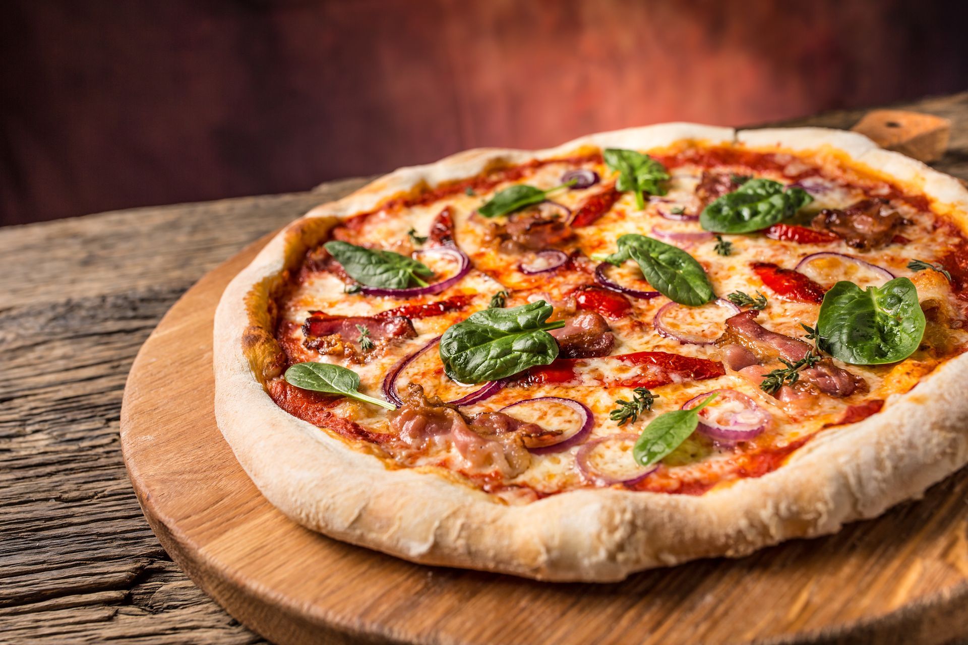 A pizza is sitting on a wooden cutting board on a wooden table.