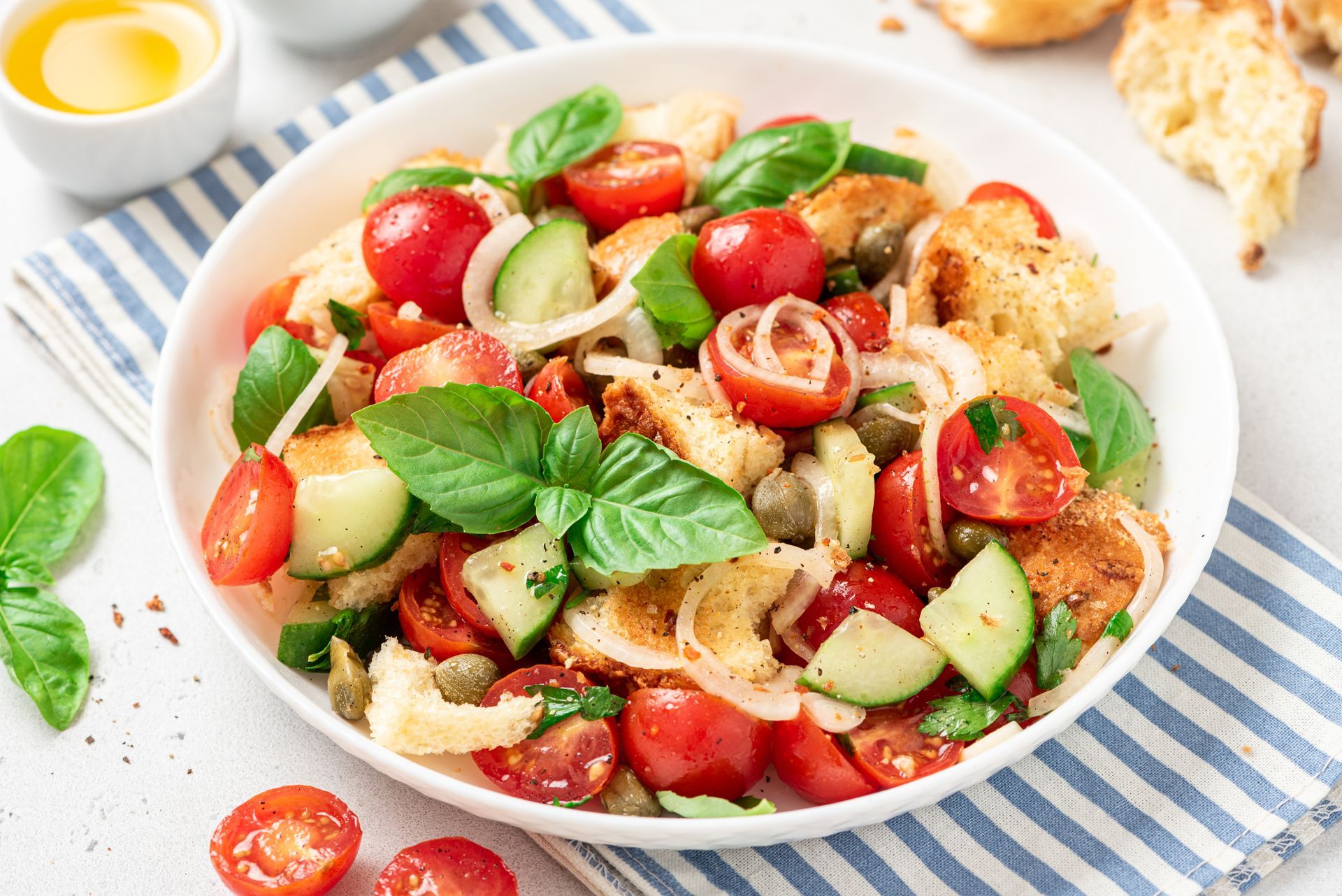 A salad with tomatoes , cucumbers , olives and bread in a bowl on a table.