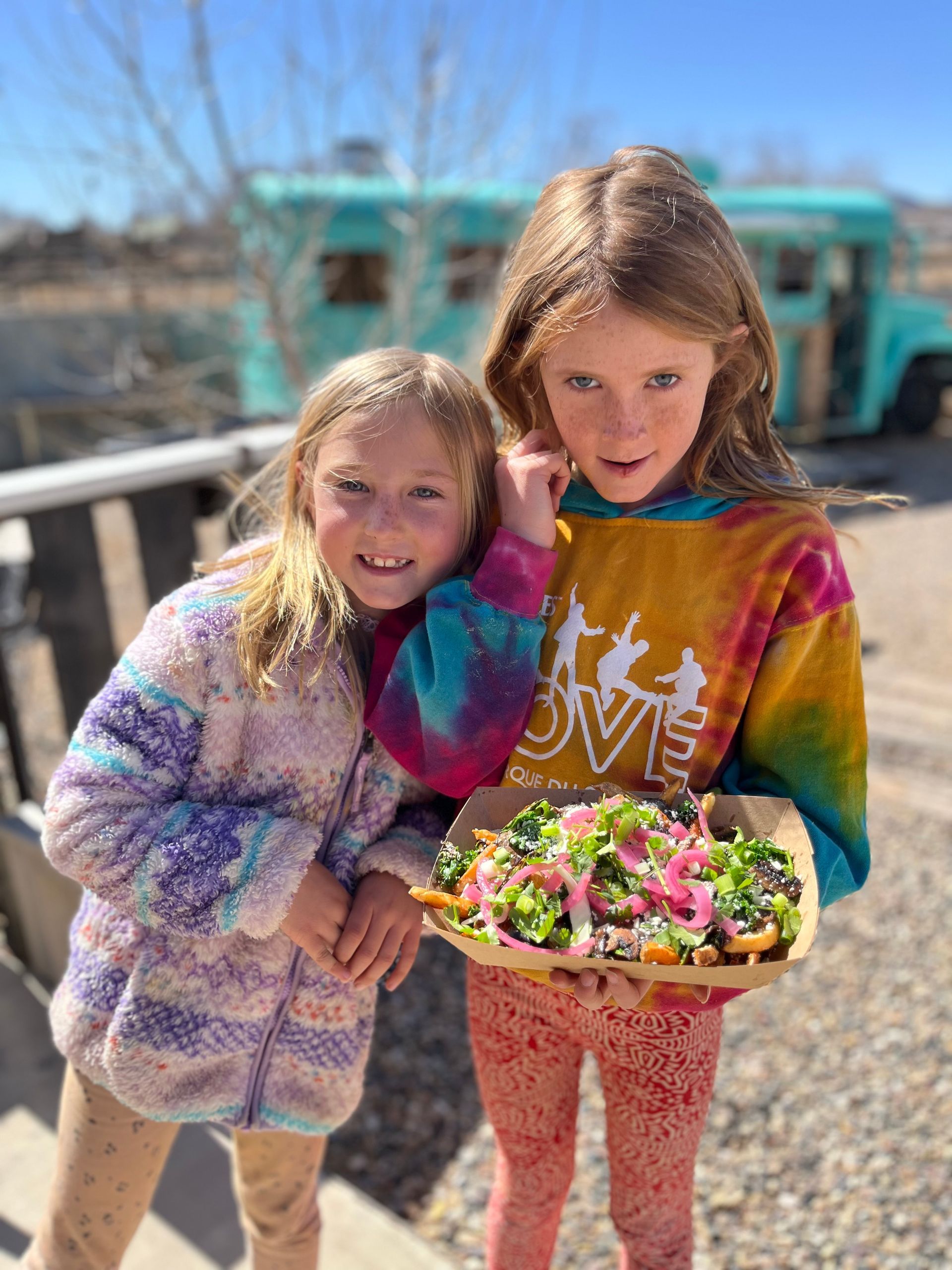 A pastry with a strawberry on top is in a paper container on a wooden table.