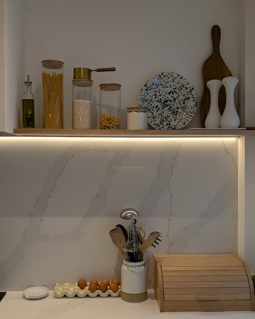 A white kitchen counter with a sink, a brass faucet, wooden kitchen tools, and a decorative egg print on the wall.