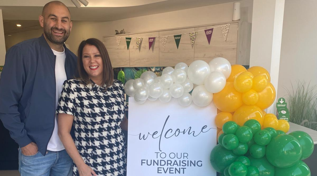 A smiling couple stands next to a sign that says 