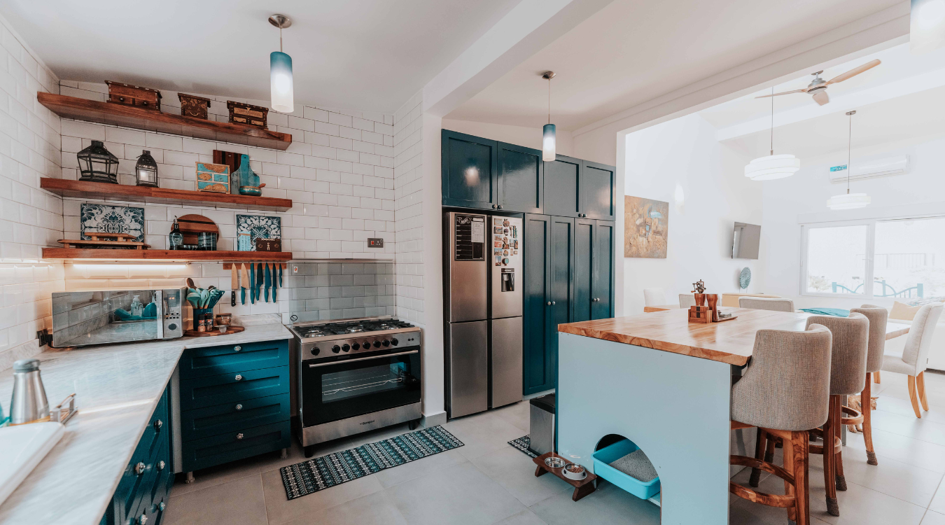 A modern kitchen featuring blue cabinetry, a stainless steel refrigerator, white brick walls, and a matching kitchen island.