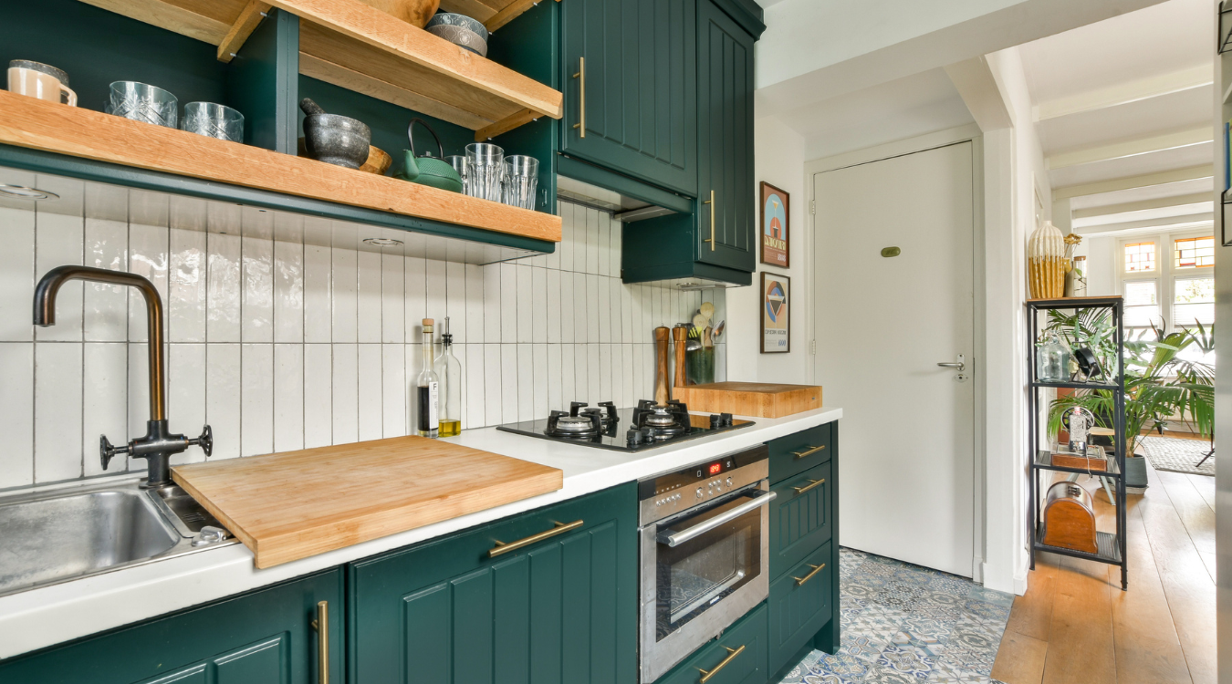 Green kitchen with wood shelves, white backsplash, and stainless steel appliances.