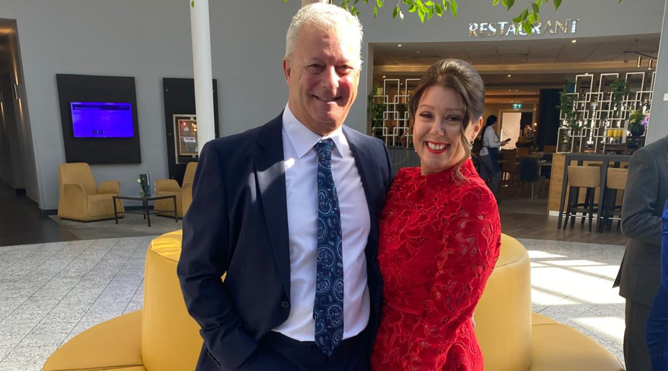 A smiling couple in formal attire standing together in a hotel lobby.
