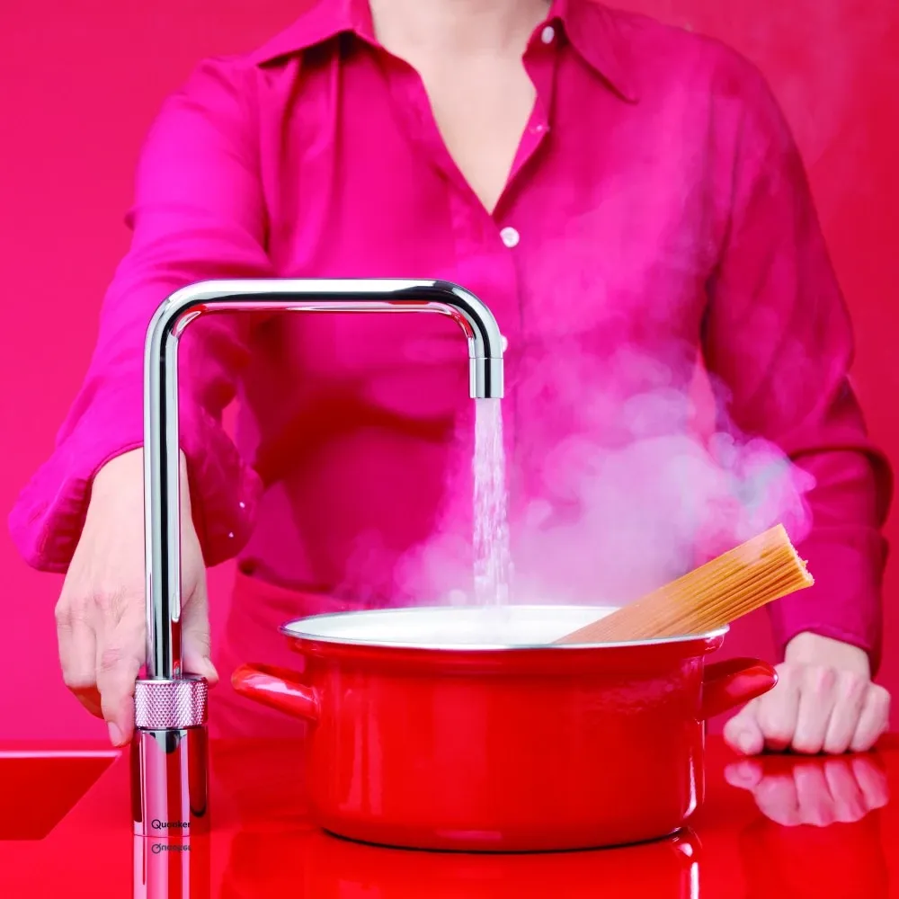 A woman in a pink shirt is pouring water into a red pot