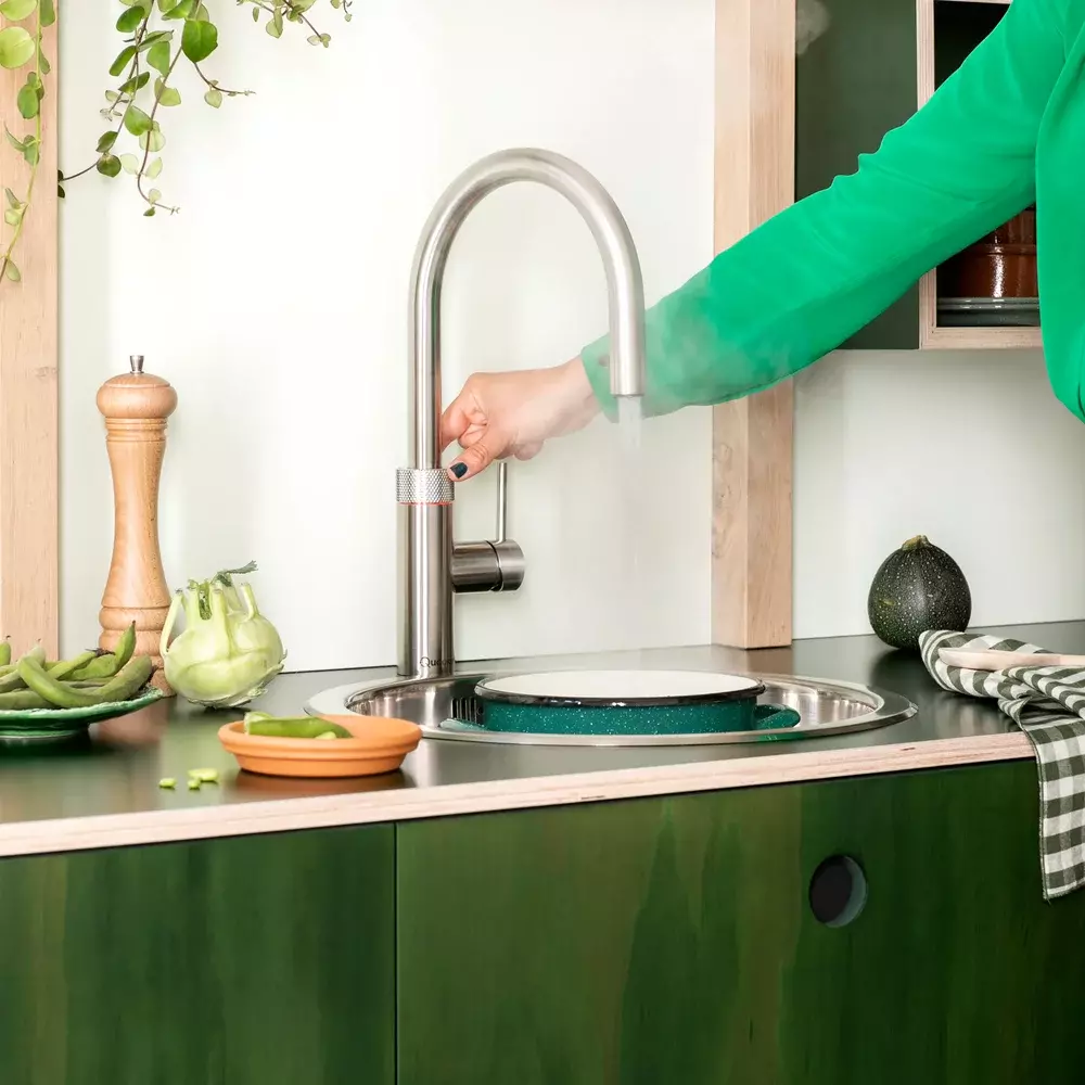 A person in a green shirt is pouring water into a sink.