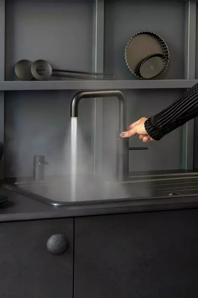 A person is pressing a button on a faucet in a kitchen.