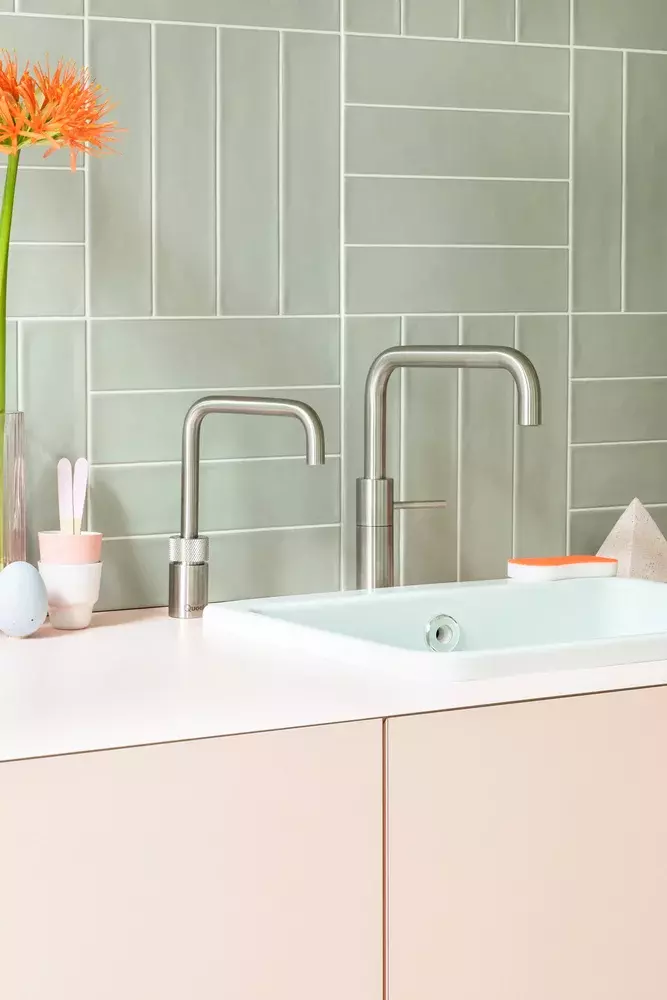 A bathroom sink with two faucets and a vase of flowers on the counter.
