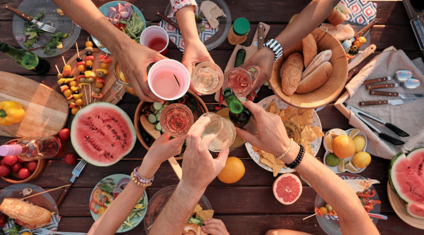 A group of people are toasting with wine glasses at a picnic table, in summer