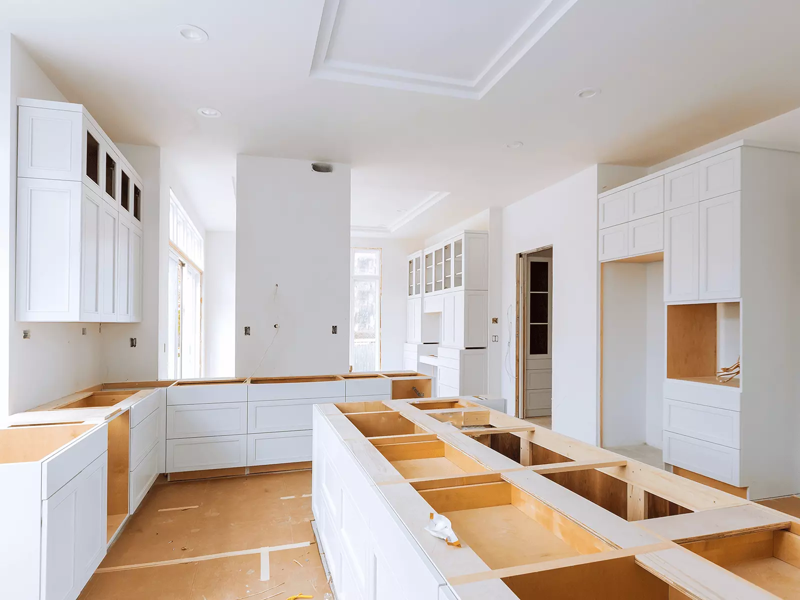 A kitchen under construction with white cabinets and wooden counter tops.