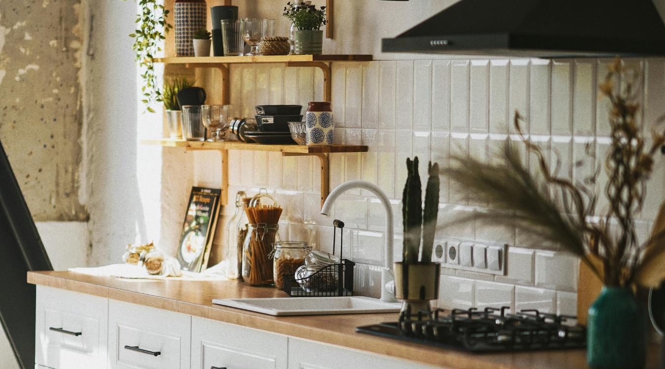 A bright, airy kitchen featuring white cabinetry, warm wooden worktops, and open shelving, with sunlight pouring in through the window. Bright kitchen with white cabinets, wooden countertops, and open shelving. Sunlight streams in from the window.