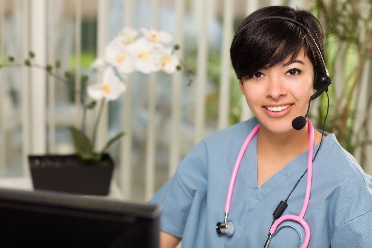 Smiling nurse in light blue scrubs wearing phone headset
