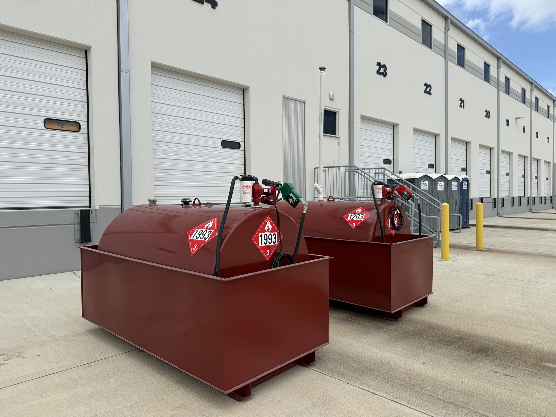 Two maroon industrial dumpsters beside a white warehouse loading dock