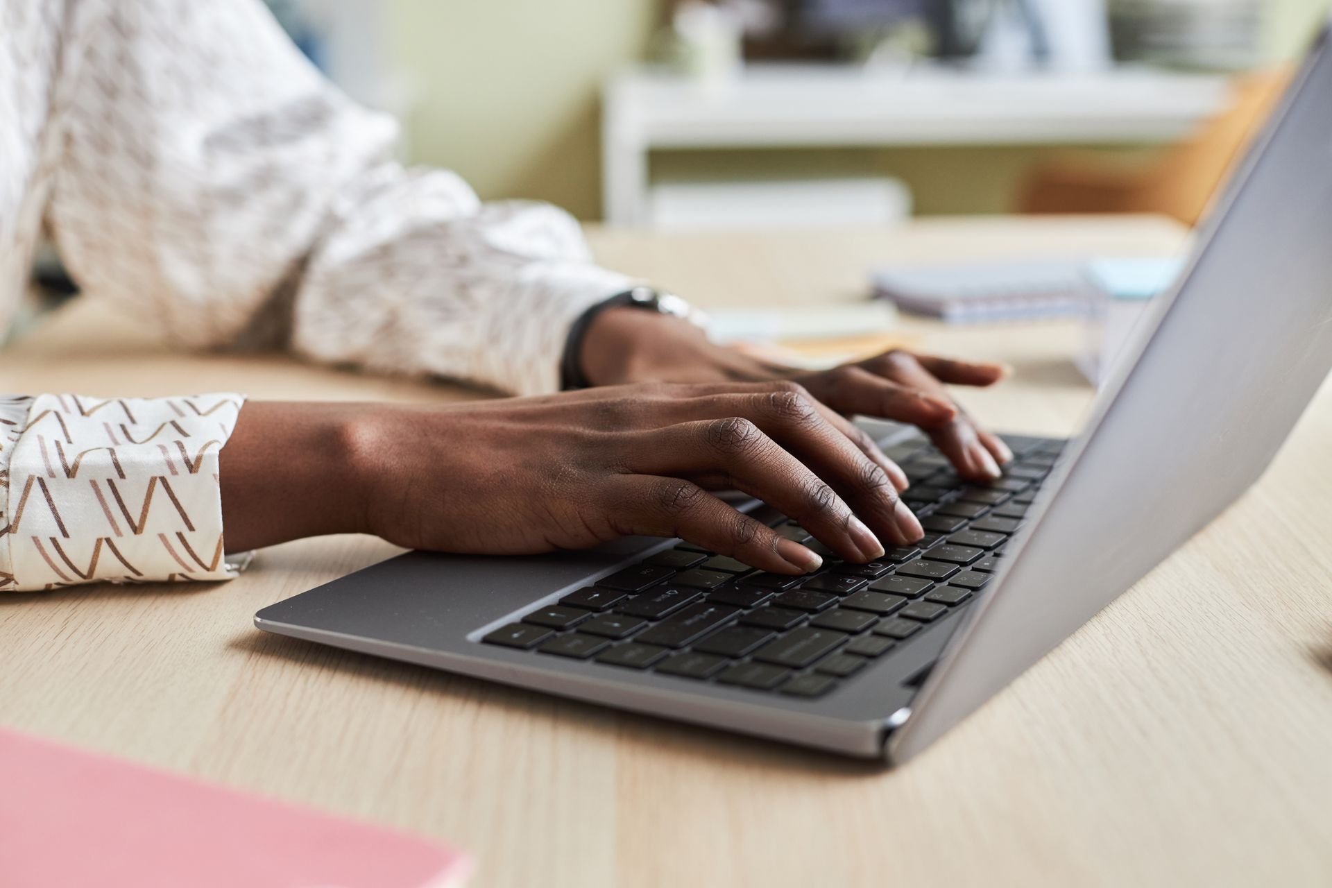 Hands typing on a laptop at a desk in a bright office setting