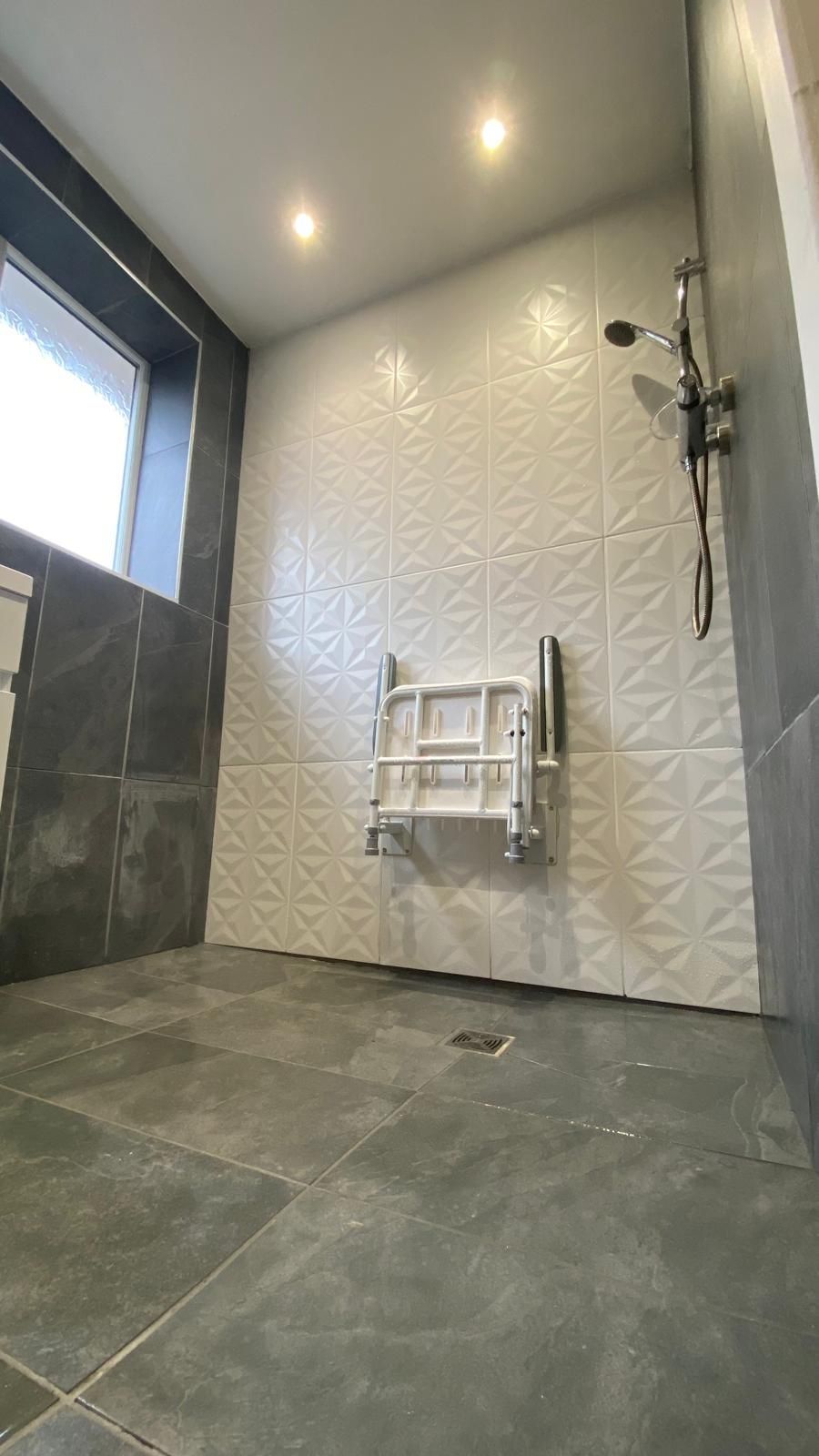 Modern bathroom with white textured tile, a shower seat, and dark gray tile flooring.