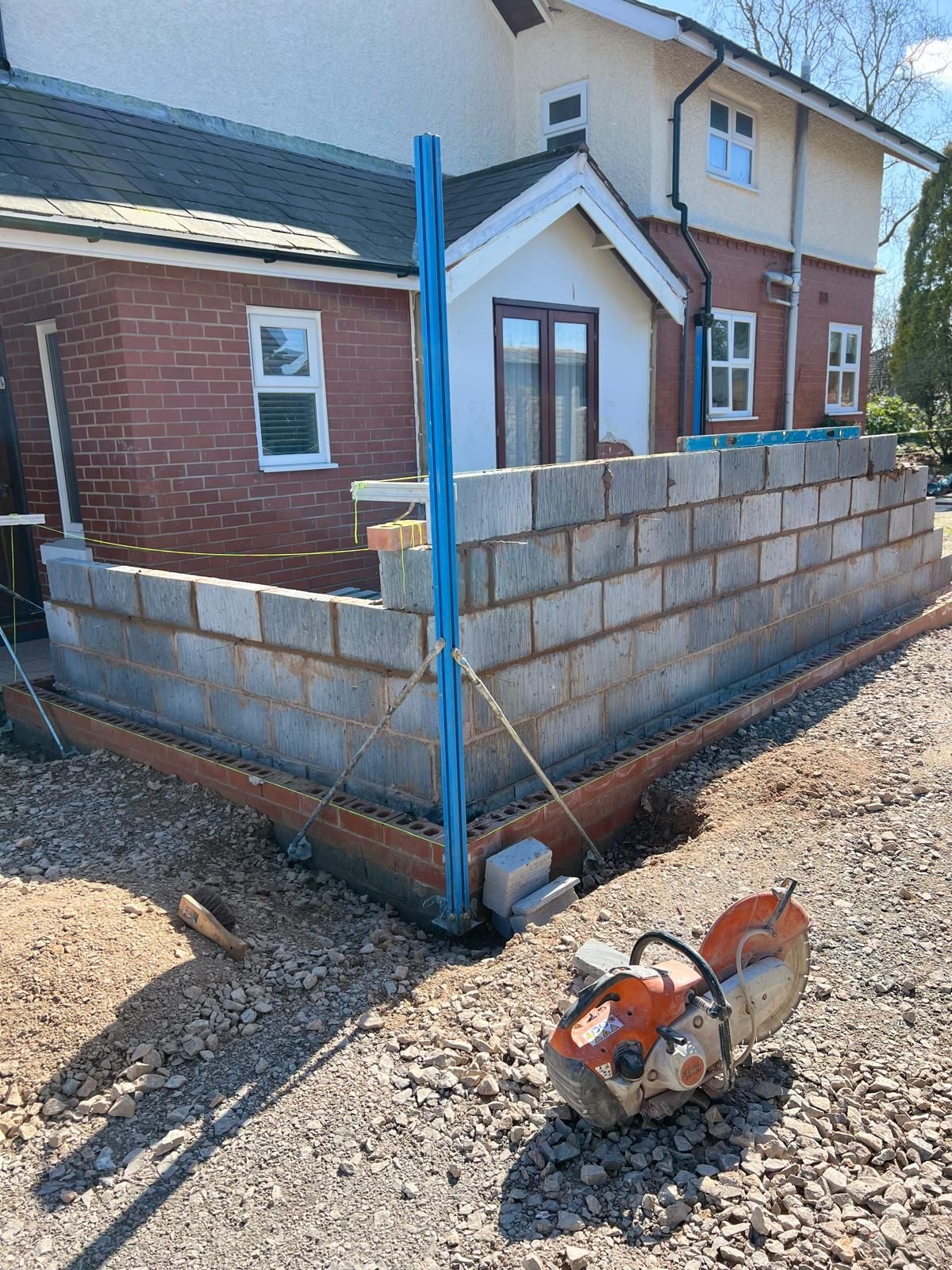 Construction site: Brick wall being built outside a house, with a saw in the foreground.