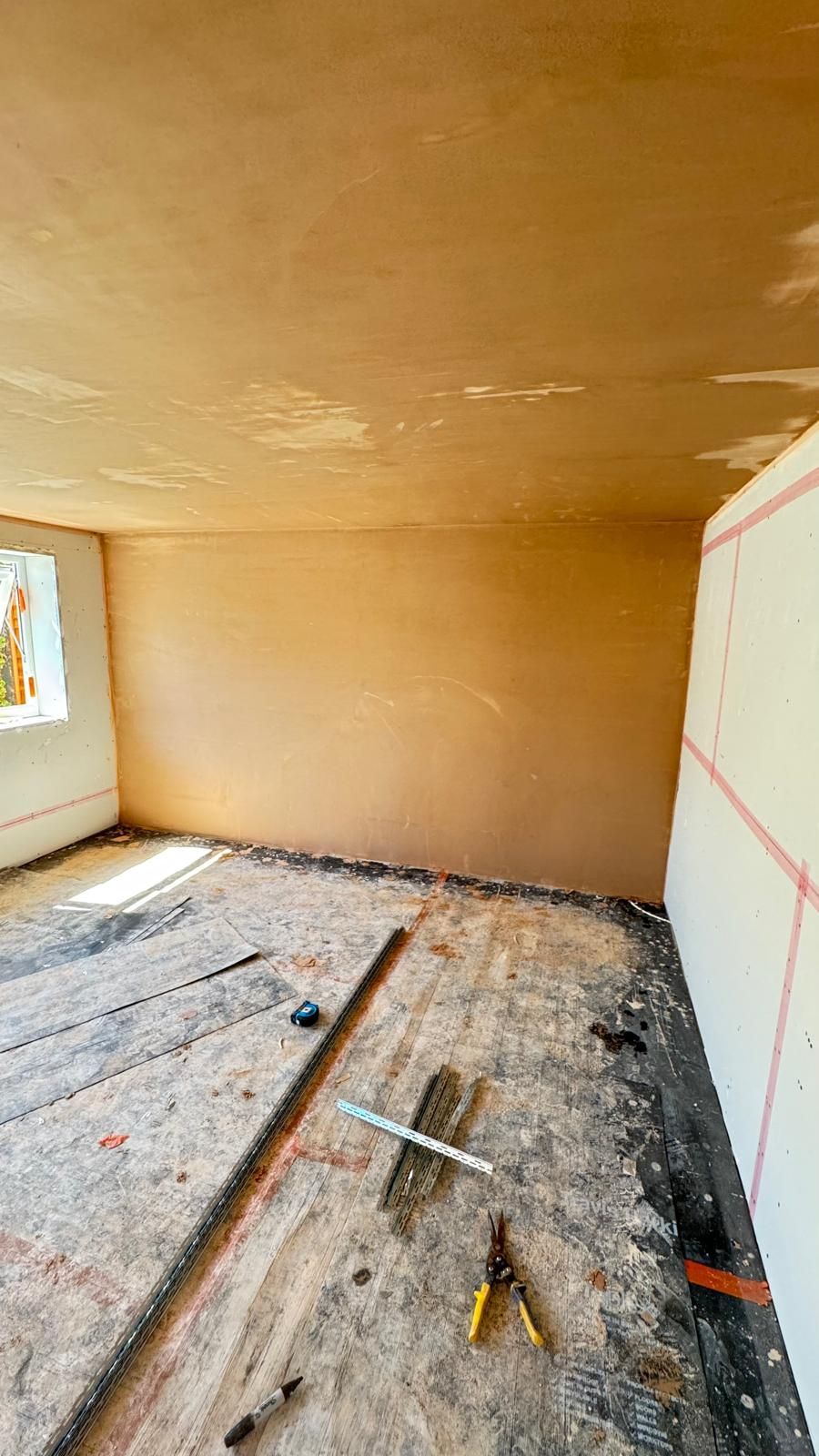 Room under construction, plaster walls and ceiling, unfinished floor, tools present.