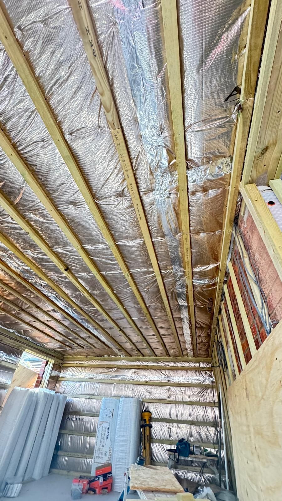 Interior view of a building under construction. Silver foil insulation lines the roof and walls. Wooden beams are visible.
