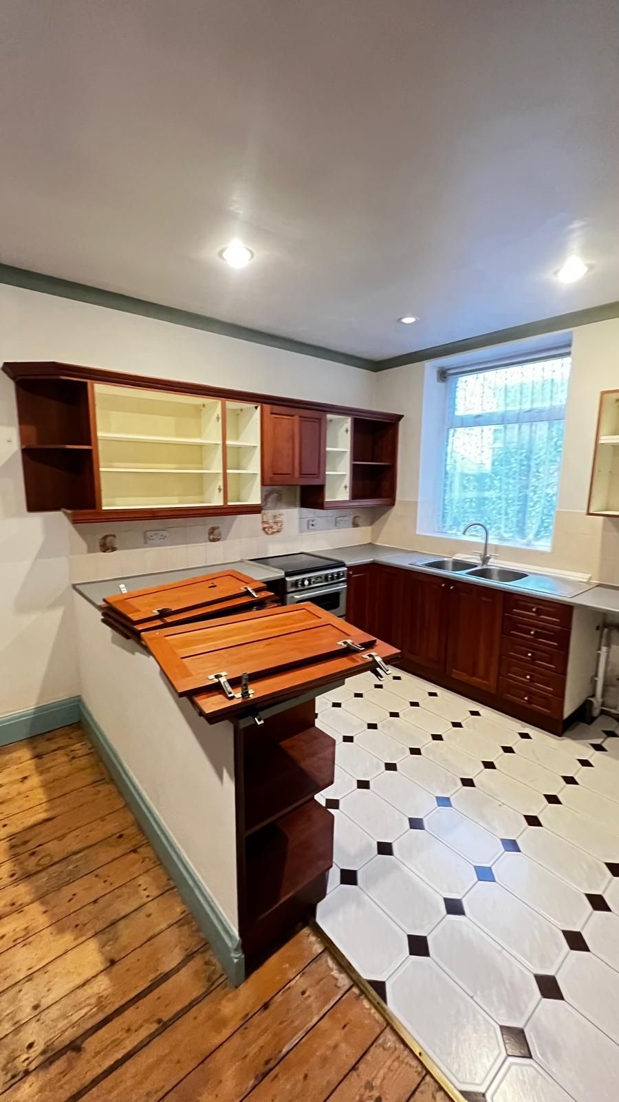 Kitchen with wooden cabinets, black and white tiled floor, and a window.