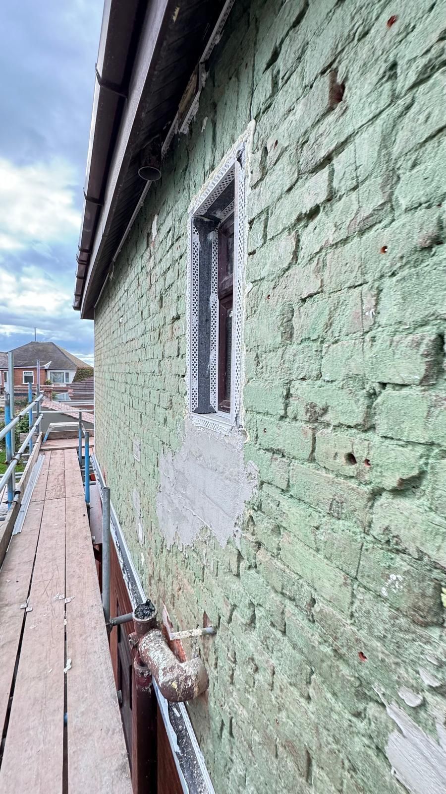 Side view of a building with scaffolding and a window. Green brick with flaking paint.