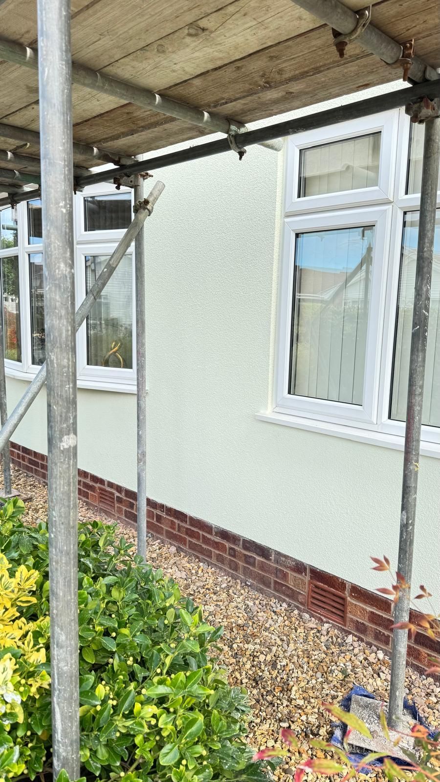 Exterior house with white windows and light stucco finish, scaffolding alongside.