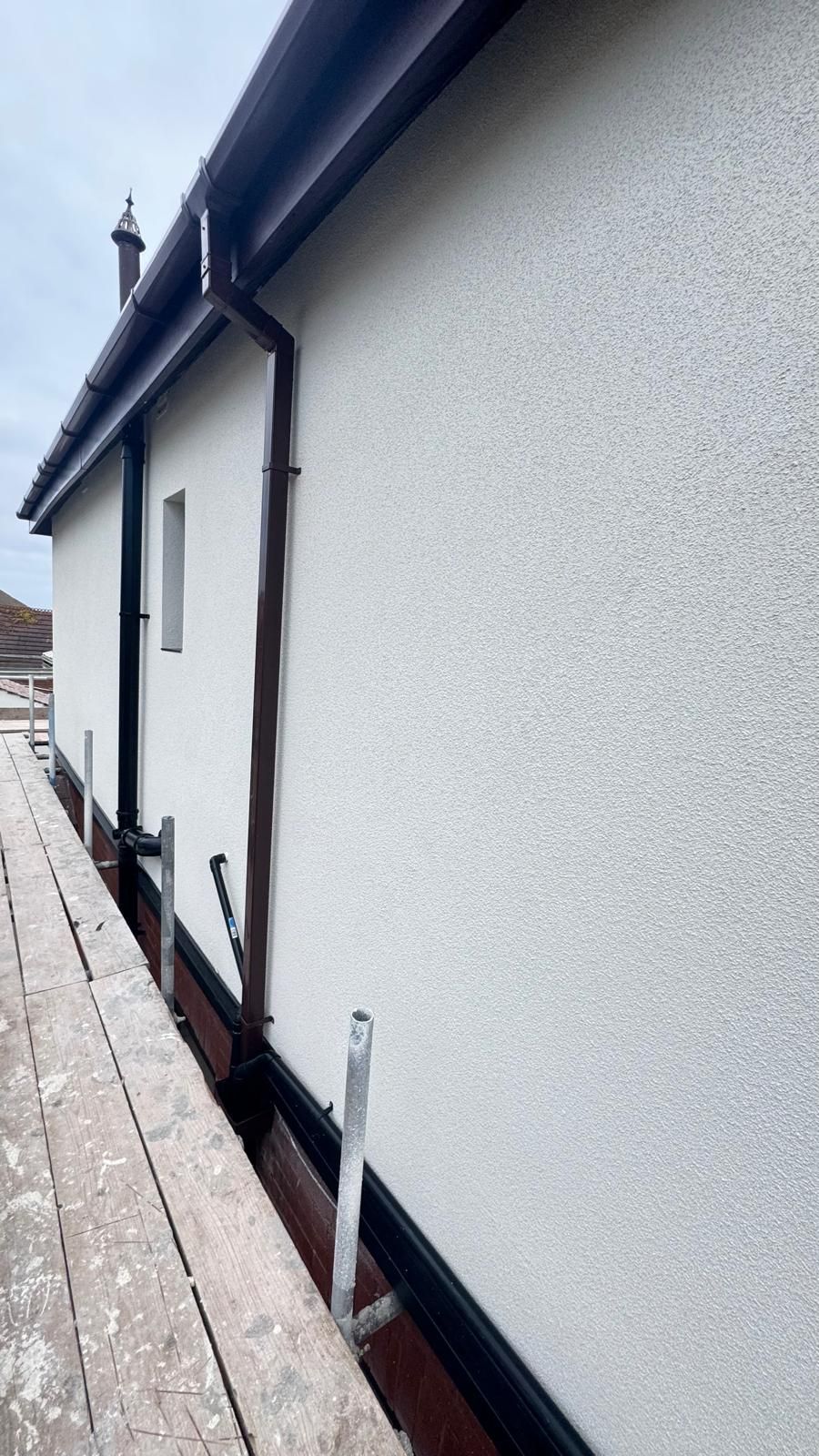 White stucco house side with dark brown gutters and trim, scaffolding below.
