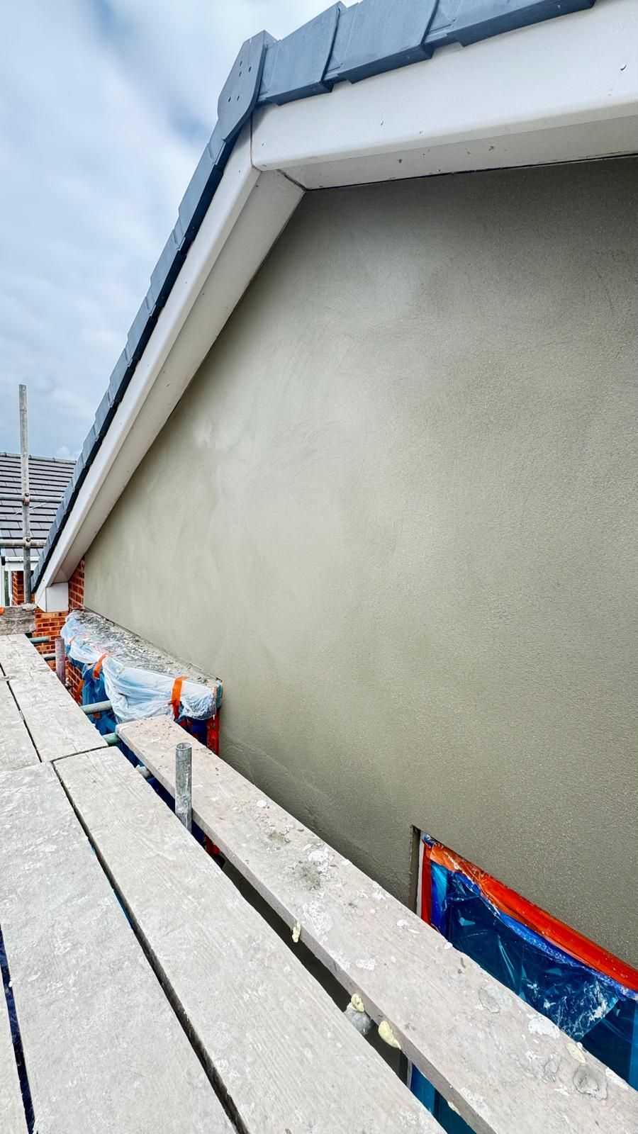 Green stucco wall under a roof with scaffolding below.