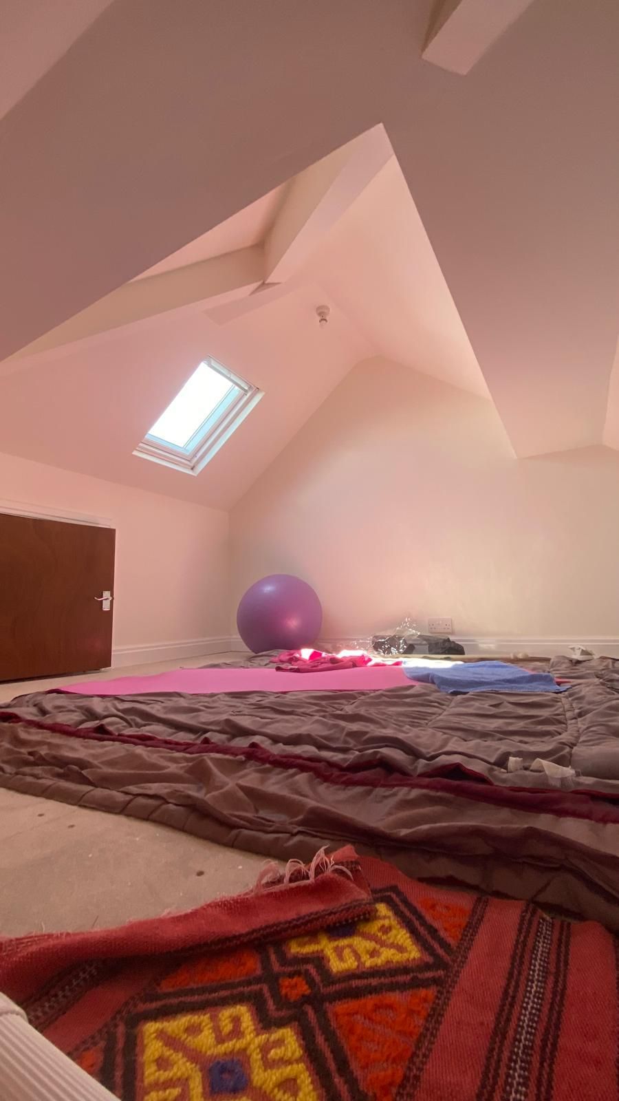 Attic space with a skylight, exercise equipment, and rugs; possibly used for yoga or relaxation.