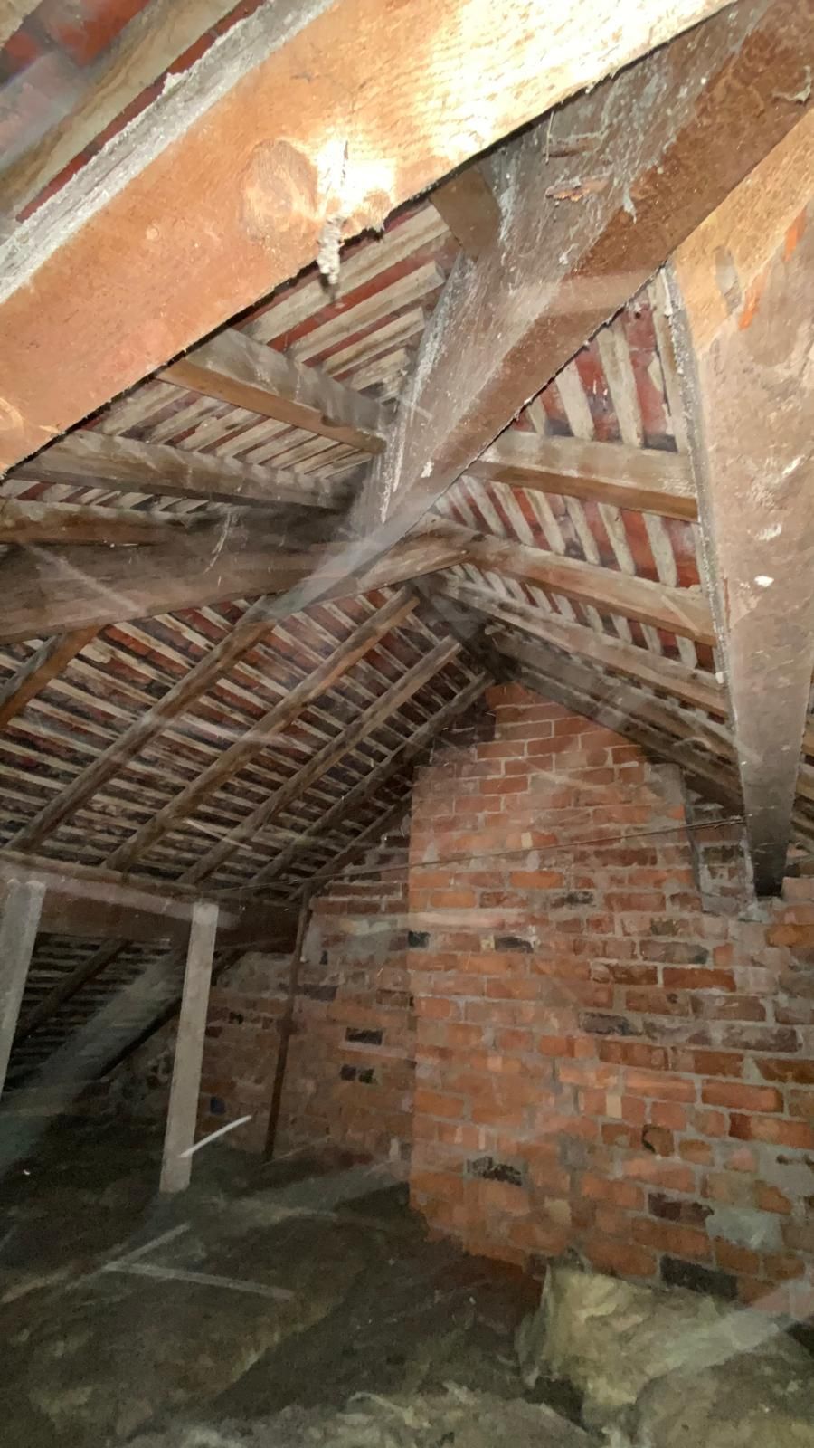 Interior of an attic with brick chimney, wooden beams, roof tiles, and cobwebs.
