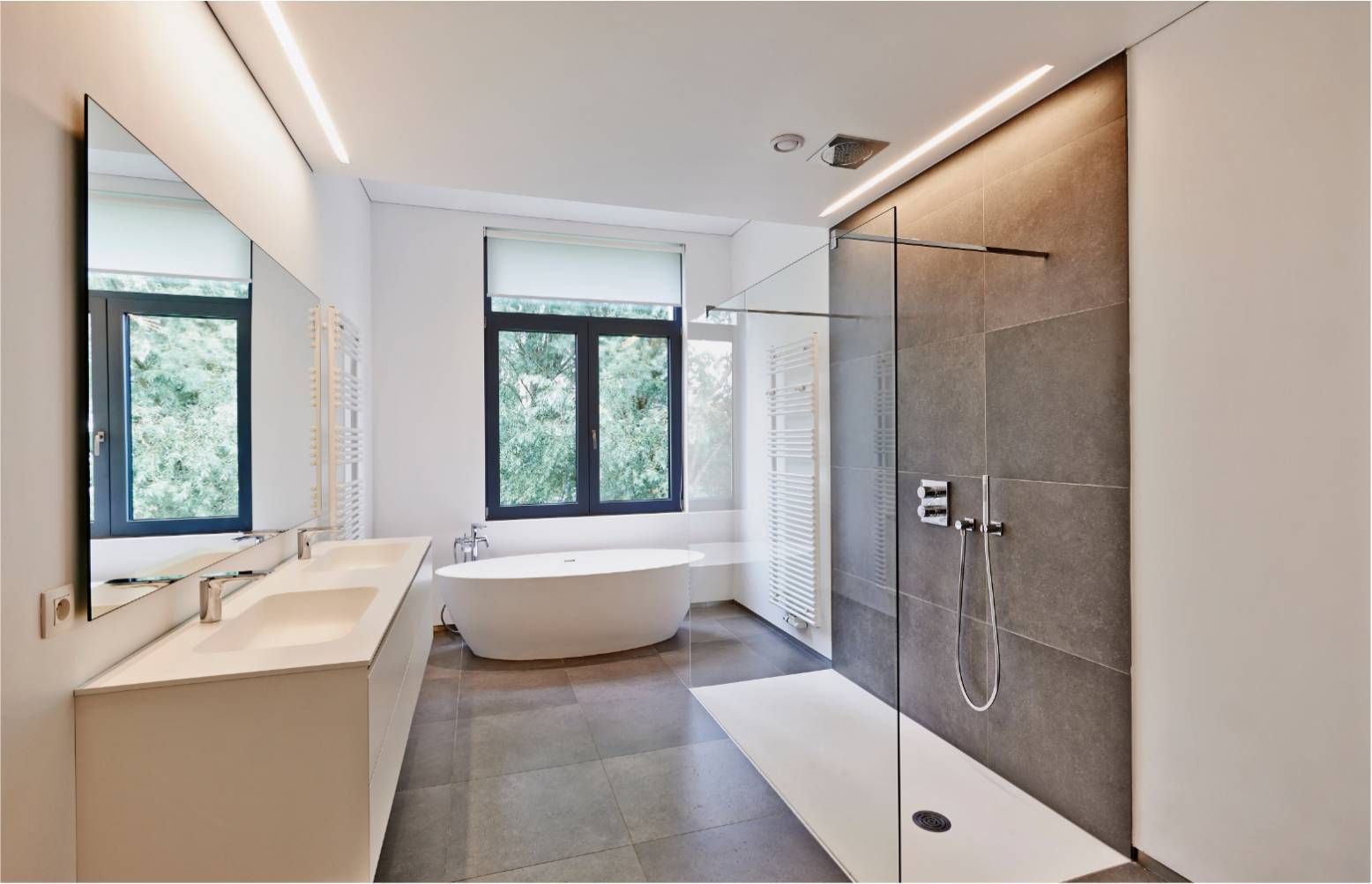 Modern bathroom with a white tub, walk-in shower, and long mirror above a double sink.