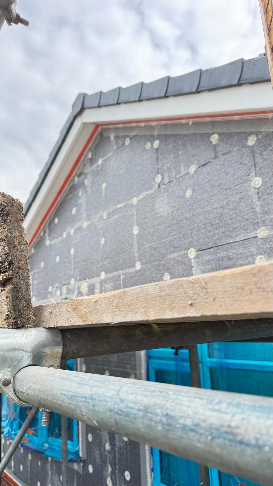 Roofline construction with gray insulation, scaffolding, and blue windows.