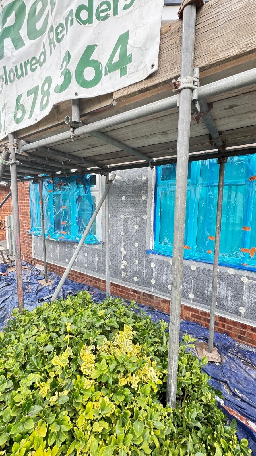 Building facade with scaffolding, covered in blue mesh, undergoing renovation.