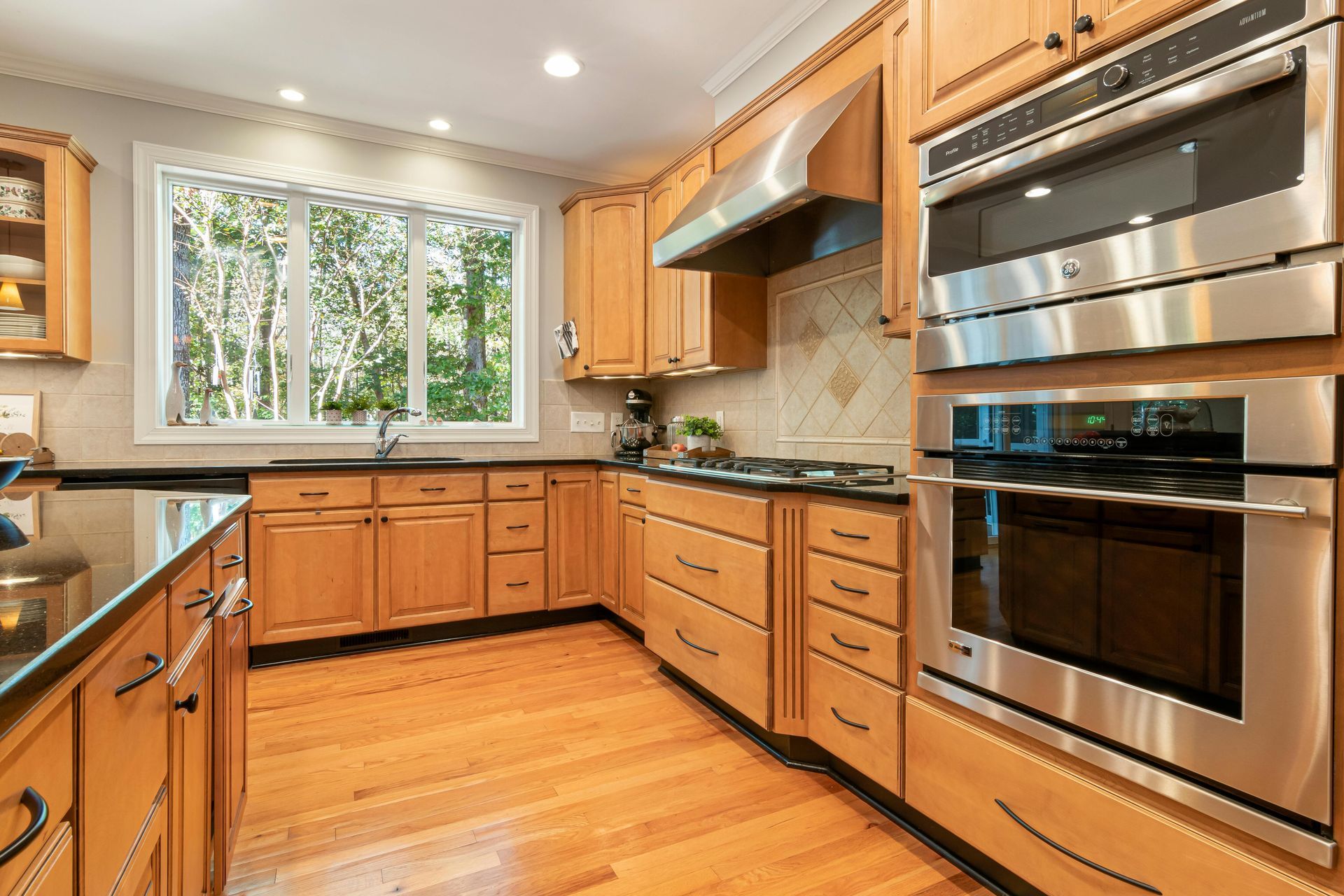 Wooden kitchen with light cabinets, stainless steel appliances, and a window overlooking greenery.