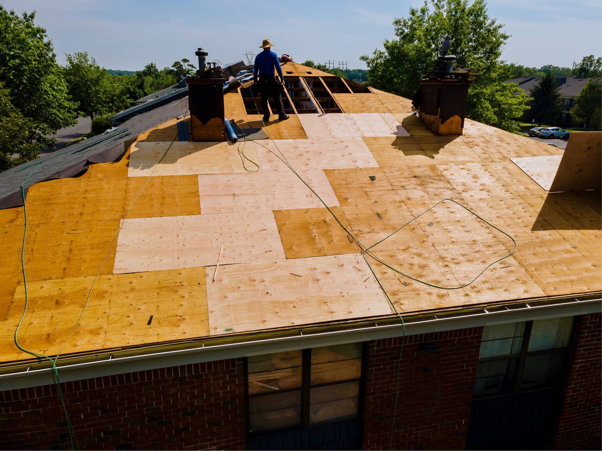 Roof partially replaced; worker stands on plywood, two chimneys visible.