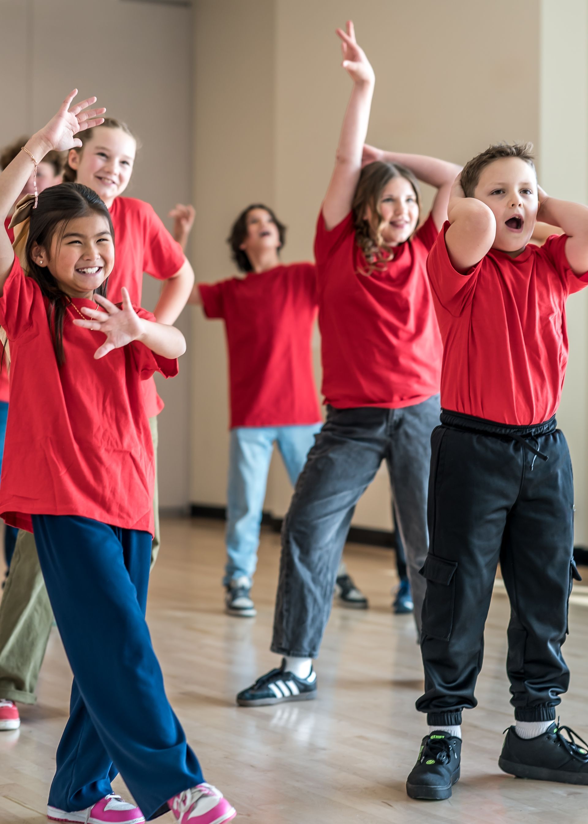 A group of students in red shirts dancing in a studio, posing with arms raised and joyful expressions.