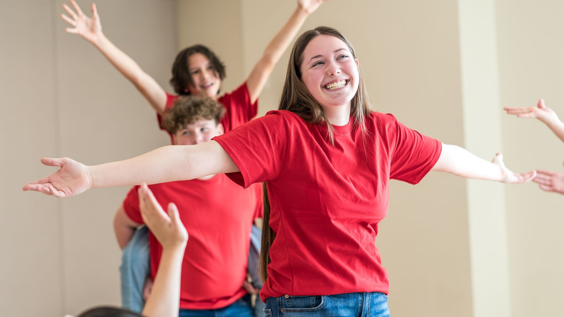 Students in red shirts stand with arms outstretched in a joyful, celebratory group gesture.