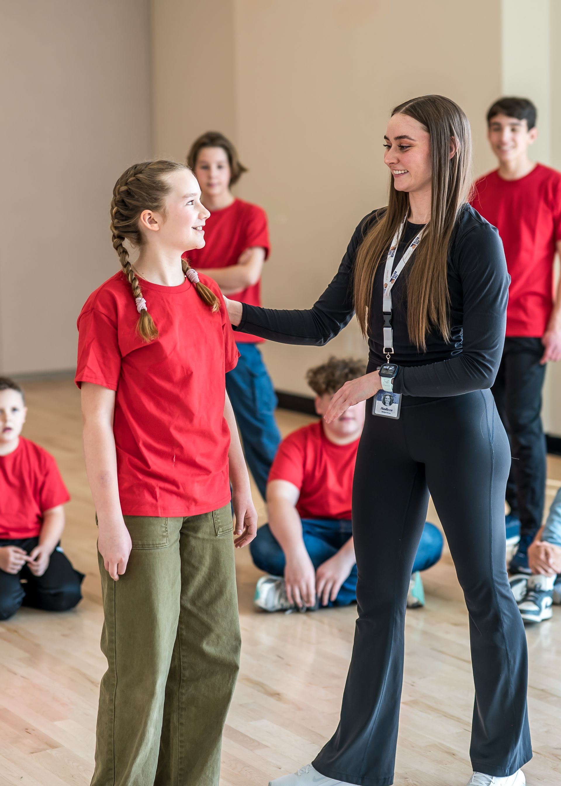 An instructor in black sportswear speaks with a student in a red shirt while a group watches in a studio setting.