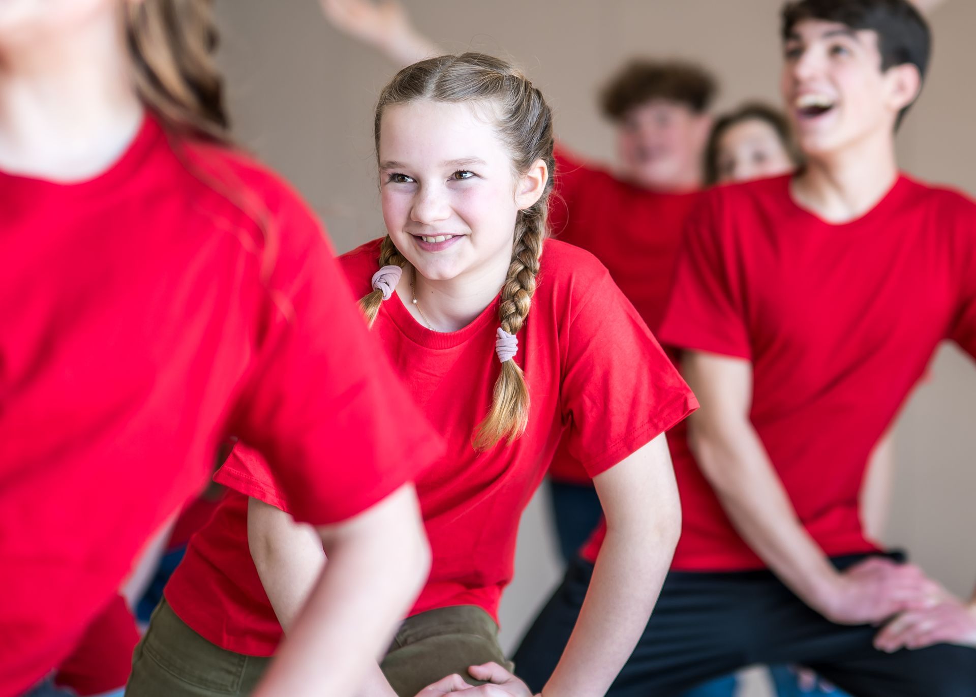 A group of students wearing red t-shirts participate in a group activity, smiling and looking in different directions.