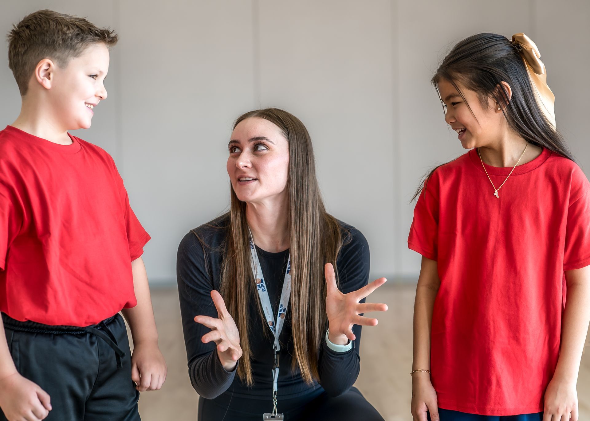 A teacher in a black long-sleeved shirt instructs two students in red shirts who are looking at them.