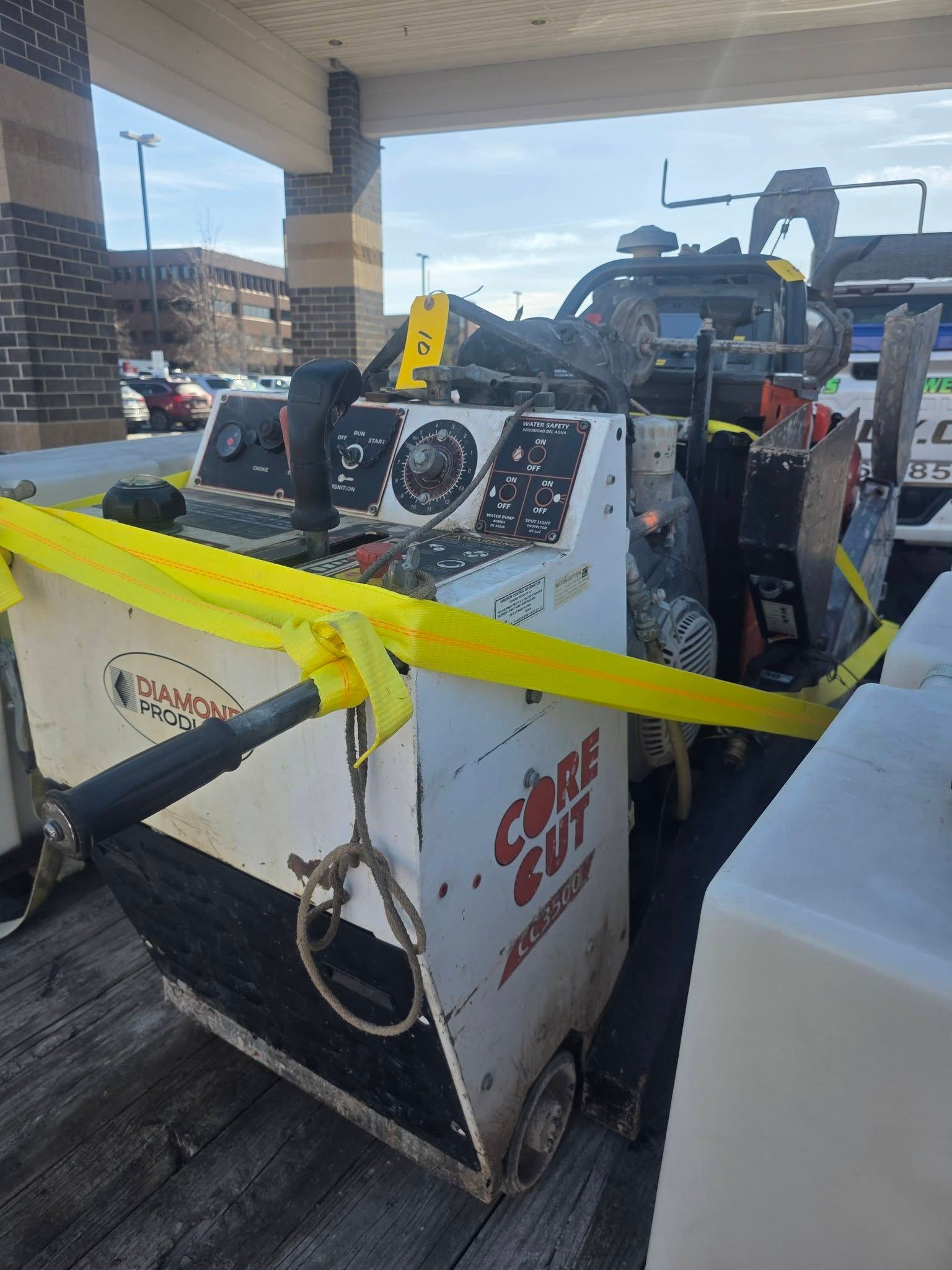A white Concrete Cut brand floor saw sits on a wooden trailer, secured by bright yellow cargo straps.