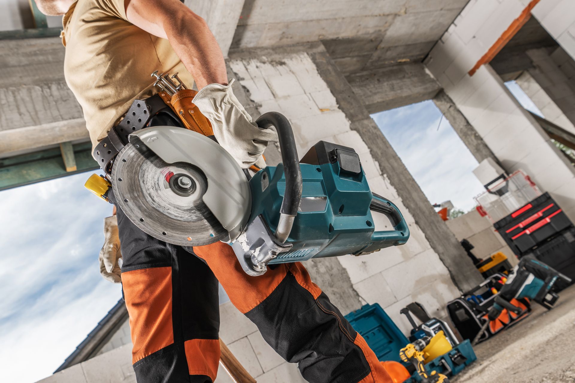 A worker in safety gear holding a teal concrete saw inside a construction site with building materials nearby.