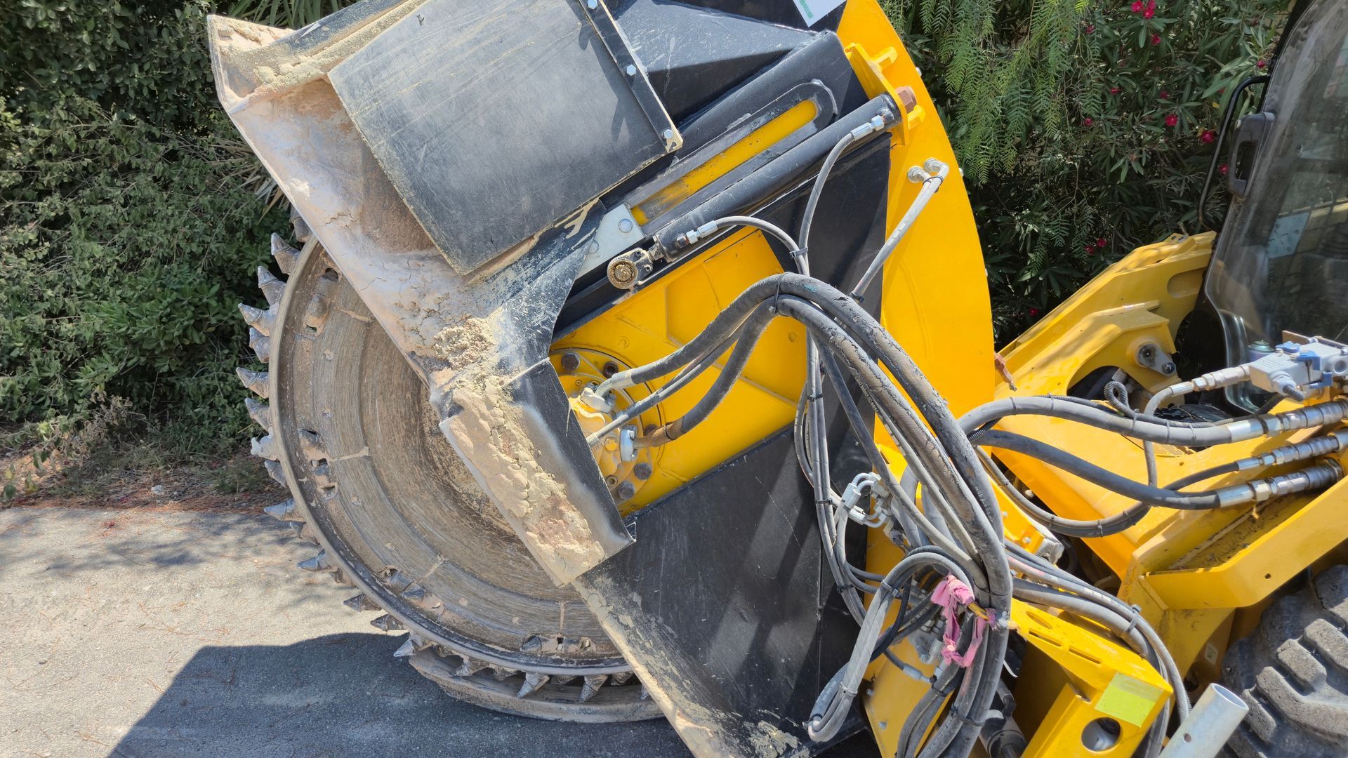 A yellow skid steer loader attachment equipped with a large, circular, toothed cutting saw for ground excavation.