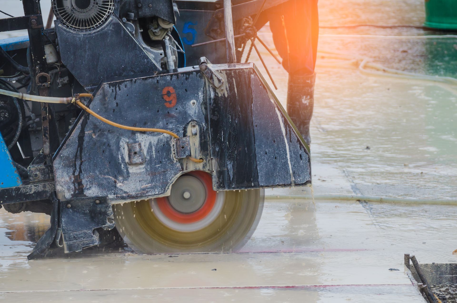 A concrete saw cutting into a wet pavement surface outdoors.