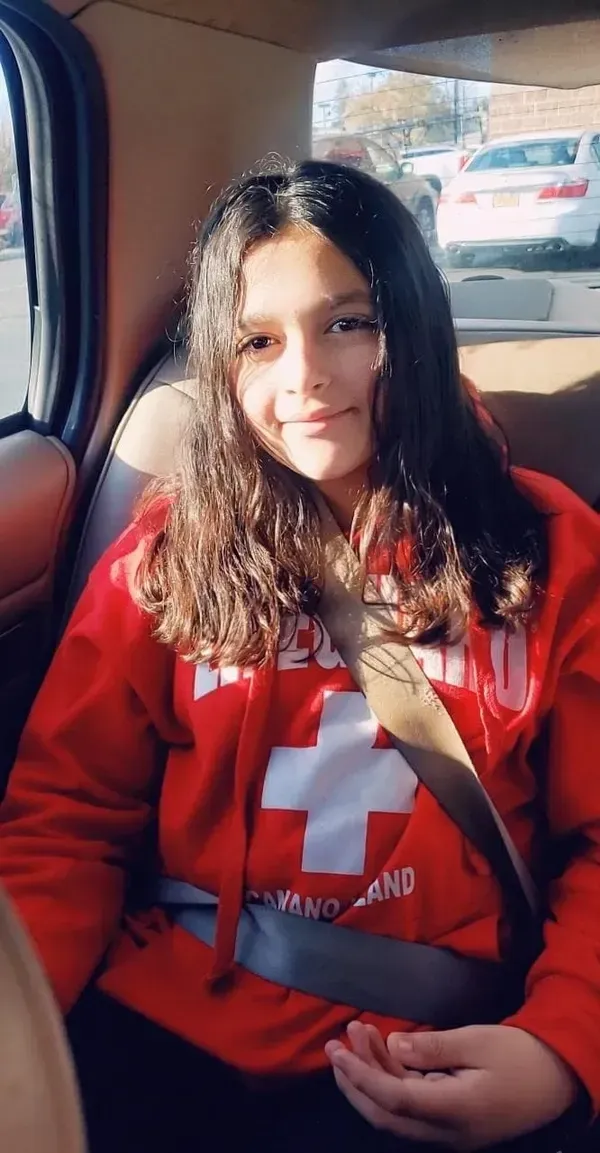 A young girl is sitting in the back seat of a car wearing a seat belt.