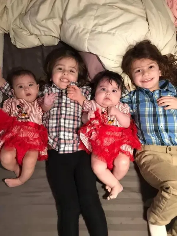 Three babies and two boys are laying on a bed.