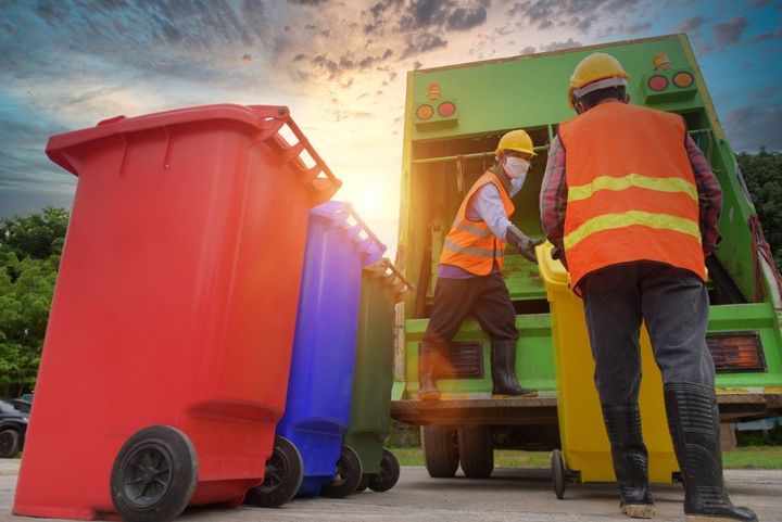 Garbage truck collecting bins. Two sanitation workers in safety vests load a yellow bin.