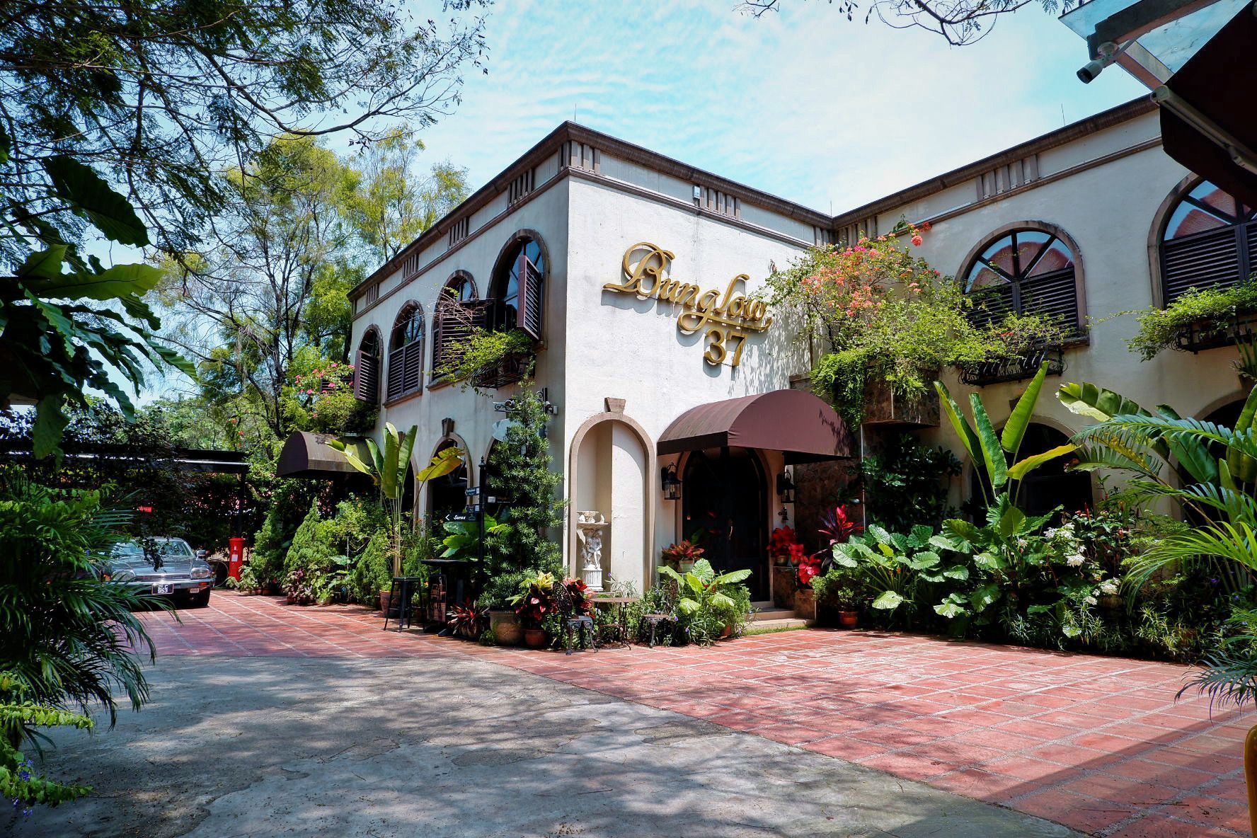 Two-story building with an arched entryway and windows, surrounded by greenery; car parked out front.