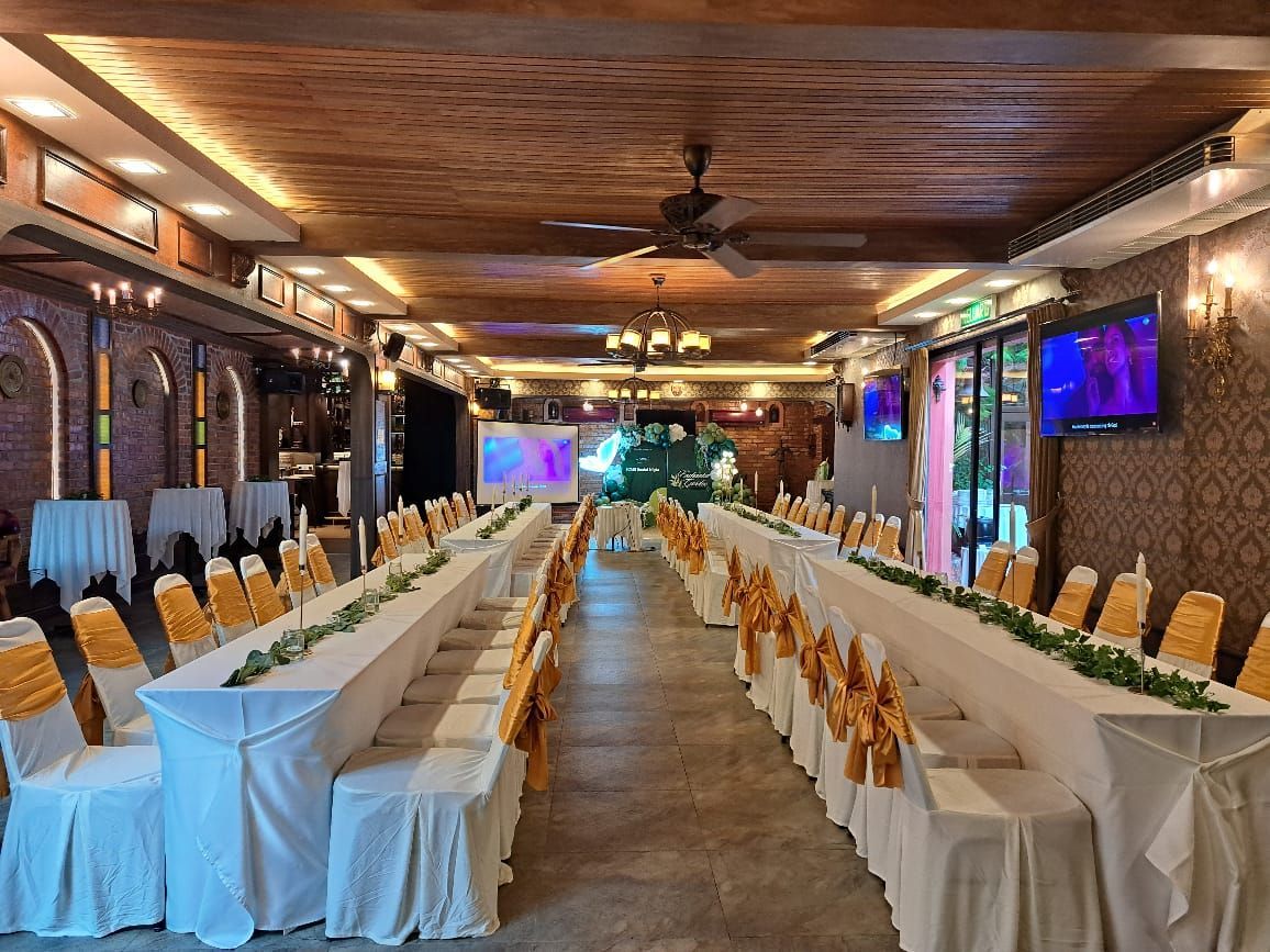 Long banquet tables set for an event, with white tablecloths and gold chair covers, in a restaurant.