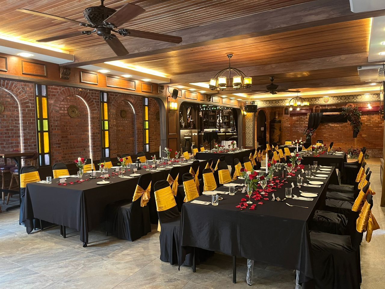 Restaurant interior with banquet tables set for an event; brick walls, wood ceiling, yellow chair sashes.